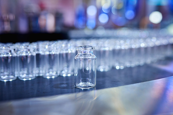 Glass vaccine vial in focus in the foreground with a group of bottles blurred out behind it
