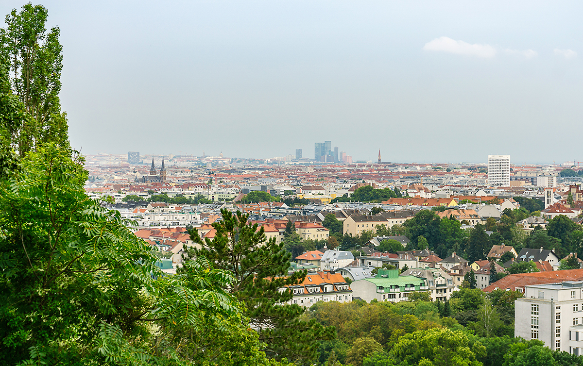 Aerial view of Vienna Austria with green trees in the forefront and orange and brown buildings spanning into the distance.