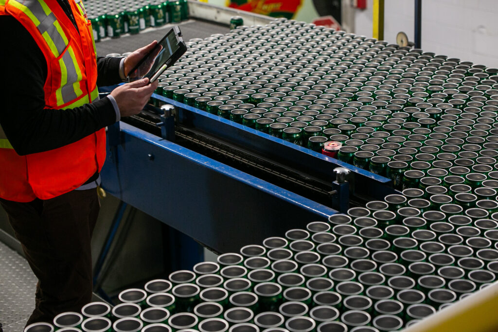 Beverage production line during lightweighting with aluminum cans on a conveyor as an operator monitors process conditions